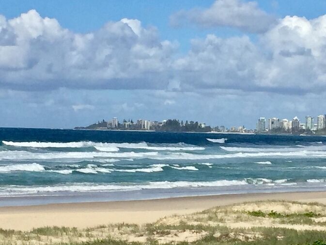 coastal view of palm beach queensland with gentle waves, sandy shoreline, and skyline in the distance, showcasing top palm beach attractions
